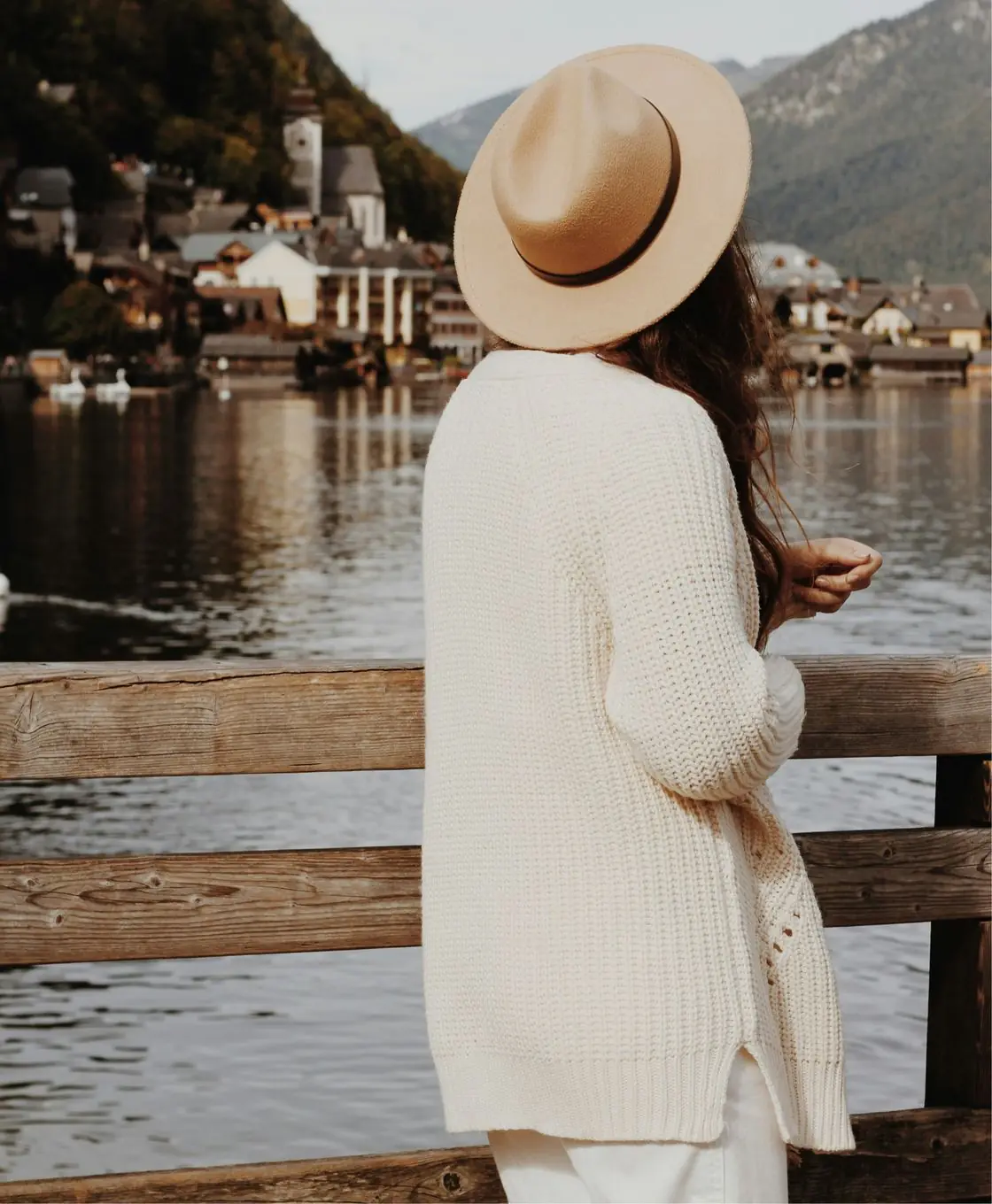 Young woman in a hat looks out over a lake in a European mountain town