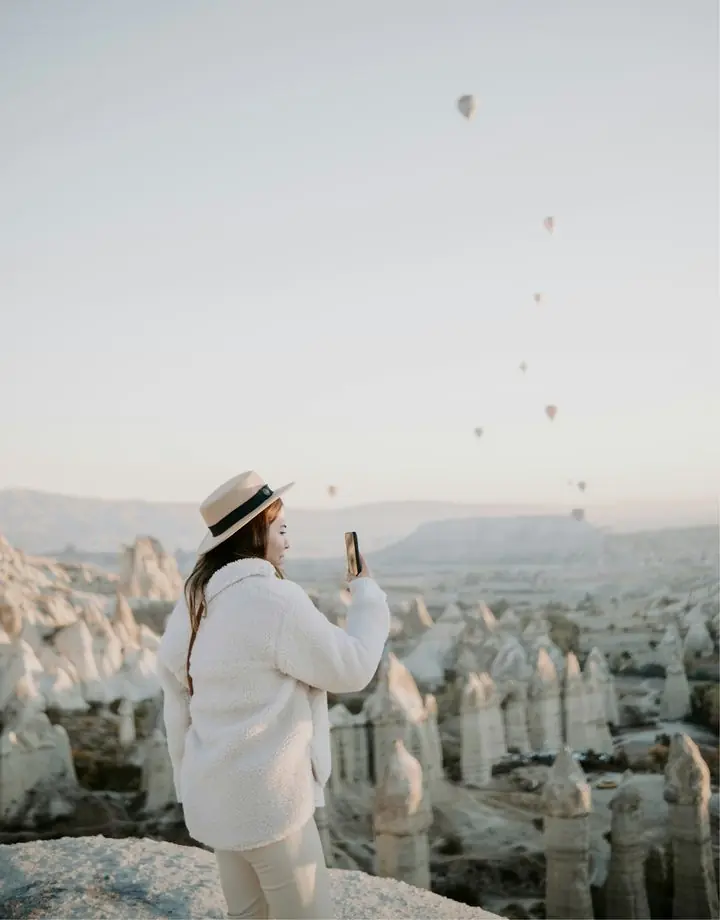 Woman in a hat photographs hot-air balloons over Cappadocia