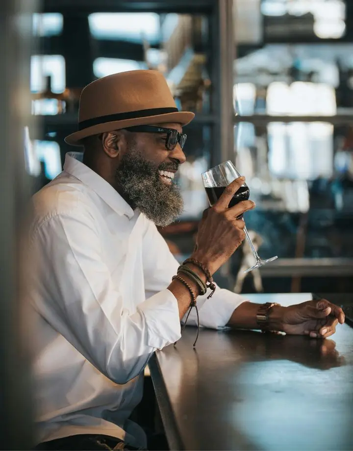 Man in a hat smiles with a glass of wine at a bar